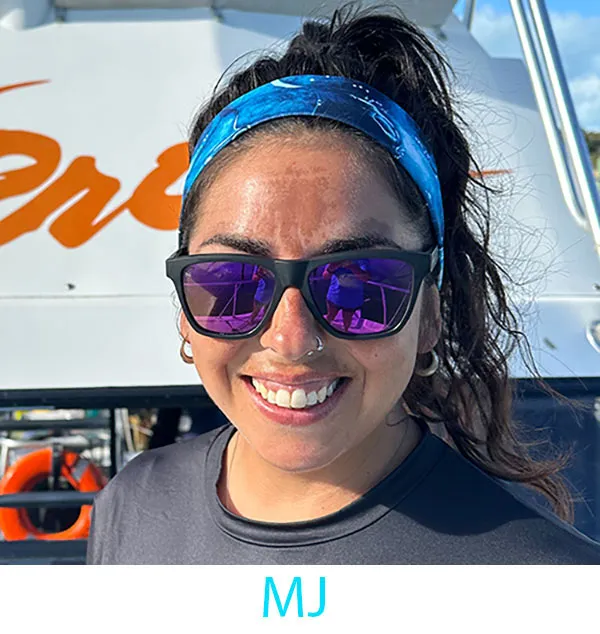Person wearing sunglasses and a blue headband smiles in front of a boat.